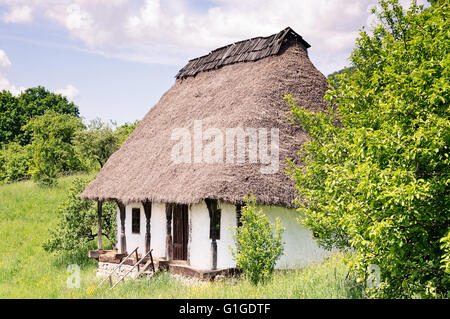 Old clay house with thatched roof, white plastered walls and wooden porch. Stock Photo