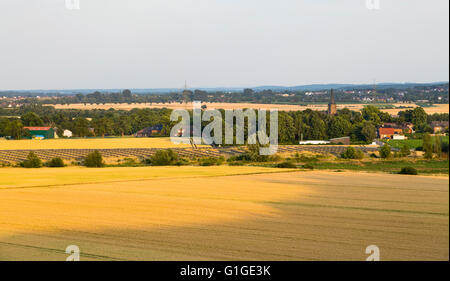 High angle view over fields to a large solar panel park providing renewable energy with a village in the background. Stock Photo