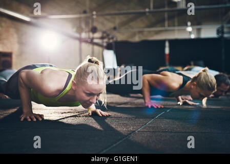Fit young woman doing pushups looking focused, working out in a gym with other people Stock Photo