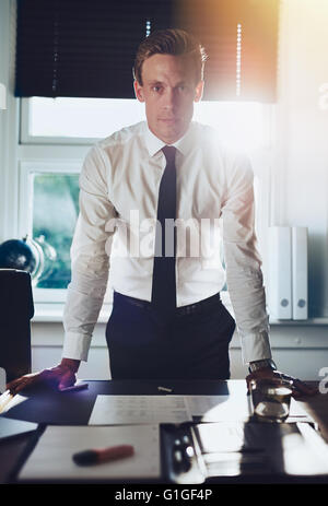 Executive business man standing at desk at office with hands resting at desk looking serious at camera Stock Photo