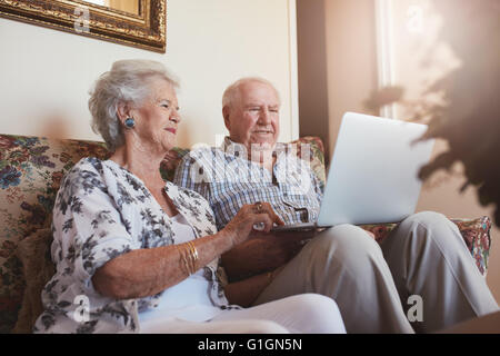 Elderly couple using laptop computer at home. Senior man and woman sitting on sofa working on laptop. Stock Photo