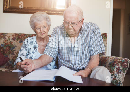 Portrait of a retired couple looking over documents while sitting at home. Senior caucasian man and woman sitting on sofa and si Stock Photo