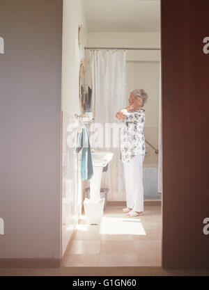 Full length indoor shot of elderly woman getting ready at dresser. Senior female getting ready in bathroom. Stock Photo