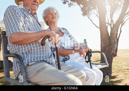 Senior couple sitting on a park bench with walking stick. Elderly couple relaxing outdoors on a summer day. Stock Photo