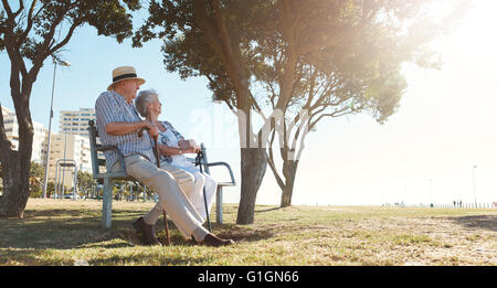 Full length outdoor shot of senior couple sitting on a bench on a summer day. Retired man and woman relaxing outdoors. Stock Photo