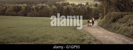 A woman and children take a woodland country walk along a dirt track by a forest Stock Photo