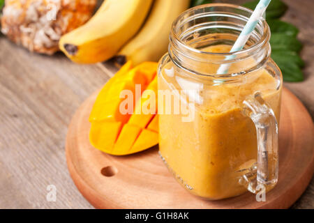 smoothie with tropical fruits: mango, banana, pineapple in a glass jar Mason on the old wooden background Stock Photo