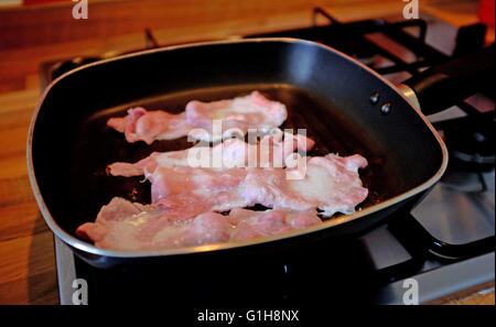 Cooking bacon slices in grill pan making a bacon sandwich in brown bread with tomato ketchup or sauce Stock Photo