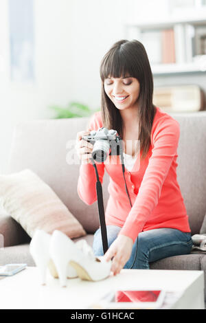 Young smiling woman taking a picture of her shoes with a camera, she is going to sell them on an online store Stock Photo