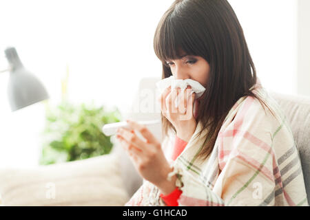 Young sick woman with cold and flu, she is blowing her nose and measuring her body temperature