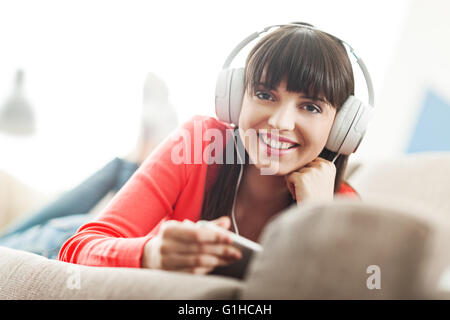 Smiling young woman relaxing at home on the couch, she is wearing headphones, using a digital tablet and watching a streaming vi