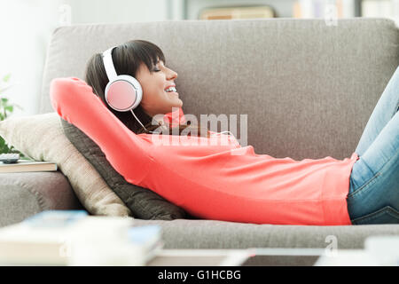 Young attractive woman relaxing on the couch at home, she is listening to music with headphones
