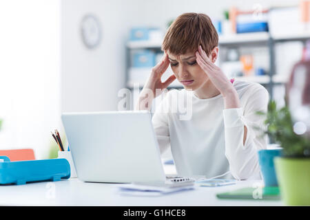 Stressed young businesswoman working at office desk, she is having an headache and touching her head Stock Photo