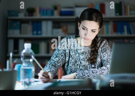 Young student girl doing her homework at home, she is writing and using a laptop Stock Photo