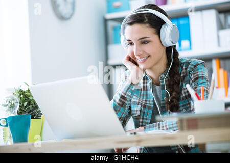Teenage smiling girl using a laptop and wearing headphones, technology and leisure concept Stock Photo
