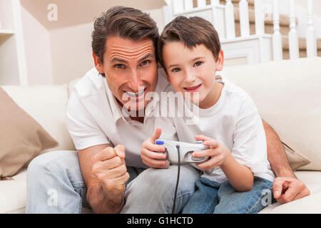 Man and male boy child, father and son having fun playing video computer console game together using handset controller on sofa Stock Photo