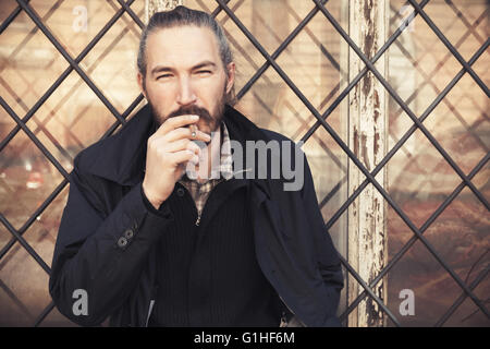 Bearded man smoking cigarette, outdoor portrait with selective focus Stock Photo