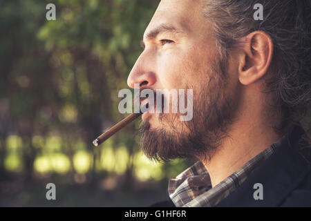 Bearded Asian man smoking cigar, outdoor profile portrait with ...