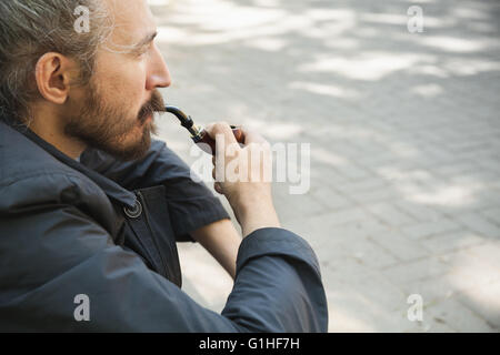 Bearded man smoking pipe, outdoor portrait with selective focus Stock Photo