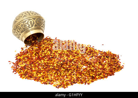 Chilli flakes spilling from a metal spice bowl isolated on a white background Stock Photo