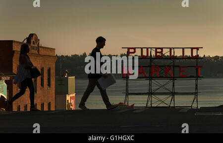 A woman and man walk in front of a sign for Pike Place Market in Seattle, Washington, USA (Adrien Veczan) Stock Photo