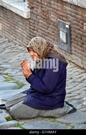 A homeless woman on the streets of Rome kneeling on the ground while praying and asking for money Stock Photo