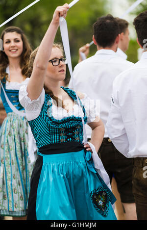 Portrait of a young woman in a dress dancing a traditional Bavarian folk dance around a maypole holding a white ribbon Stock Photo