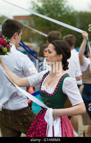 Portrait of young woman in a dress dancing a traditional Bavarian folk dance around a maypole holding a white ribbon and flowers Stock Photo