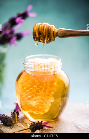 honey comb dripping from dipper into jar with nuts on old wooden table.  Healthy eat Stock Photo by lyulkamazur