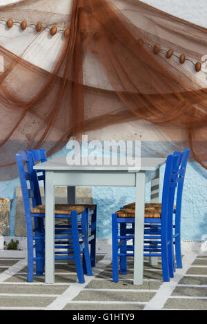 Set of  blue chairs, cyan empty tavern table on chequered floor & hanging fishing nets wall decoration.Myrina, Limnos Greece. Stock Photo