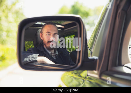 Serious Asian man as a driver looks in car mirror, outdoor summer portrait Stock Photo