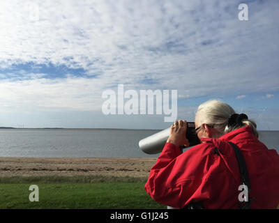 Senior Woman on beach looking through binoculars, Esbjerg, Denmark Stock Photo