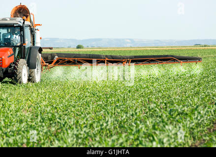Farmer in red tractor spraying soybean field with herbicides, pesticides and fungicides Stock Photo