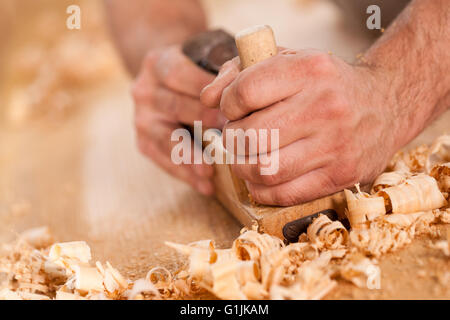 closeup of woodworker's hands shaving with a plane in a joinery workshop Stock Photo