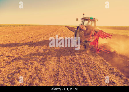 Farmer plowing stubble field with red tractor, photo manipulated to achieve old cross processing xpro look. Stock Photo