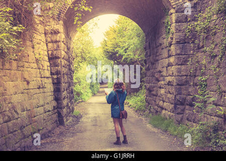 A young woman is lost in a forest below a railway bridge and is studying a map Stock Photo