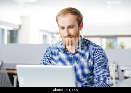 Concentrated bearded young businessman working with laptop in office Stock Photo