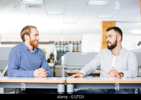 Two cheerful attractive businessmen sitting and talking at the table in office Stock Photo
