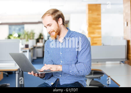 Cheerful handsome bearded businessman holding laptop and typing Stock Photo