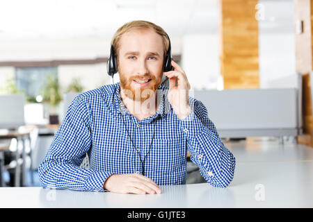 Portrait of smiling bearded man sitting on workplace and using headset Stock Photo