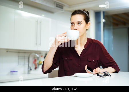 Beautiful young woman sitting and drinking coffee on the kitchen Stock Photo