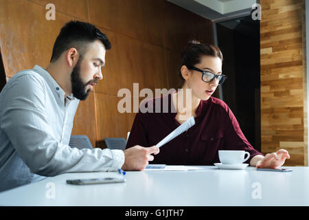 Two concentrated young businesspeople discussing new project and using smartphone in meeting room Stock Photo