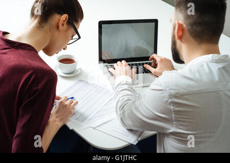 Back view of two focused serious businesspeople using laptop together in meeting room Stock Photo
