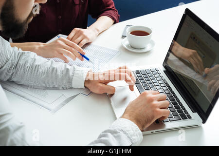 Closeup of hands of two young businesspeople typing on laptop and working together at white table Stock Photo