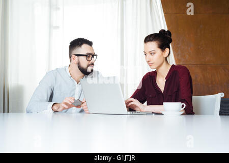 Two concentrated young businesspeople working with laptop in meeting room together Stock Photo