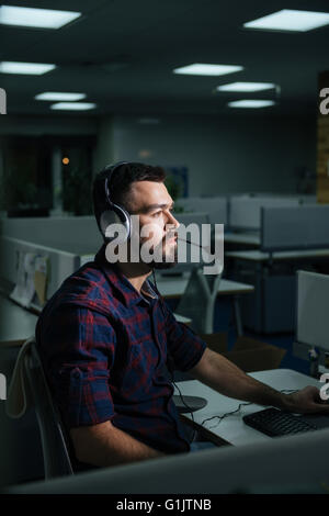 Serious bearded young businessman in headphones working in office late Stock Photo