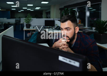 Handsome bearded young businessman sitting on workplace and working late Stock Photo