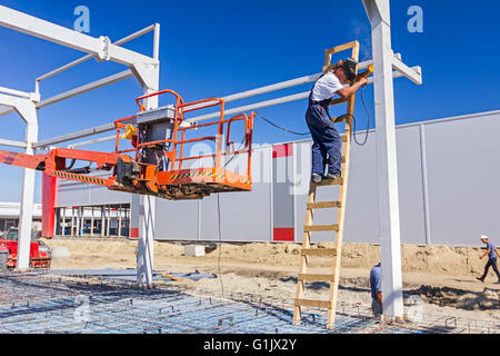 Construction worker is welding metal frame without proper safety equipment on wooden leaders. Stock Photo