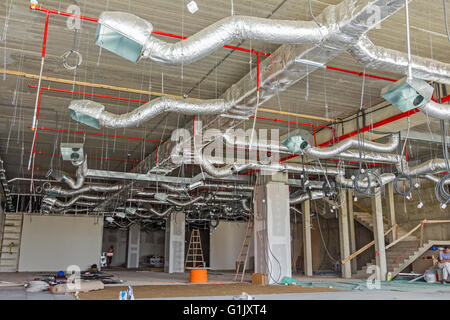 Ventilation pipes in silver insulation material hanging from the ceiling inside new building. Stock Photo