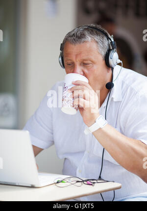 Man Drinking Coffee and Using Laptop at Cafe Stock Photo